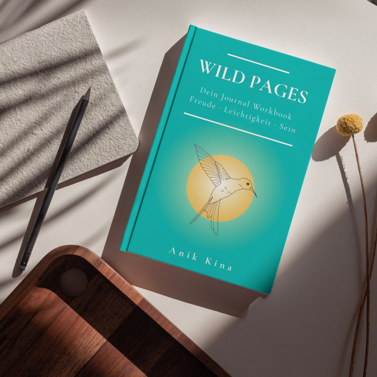 Türkisfarbenes Buch „Wild Pages“ mit Vogelillustration, daneben Stift, Filzstoff und Holztablett auf hellem Hintergrund.