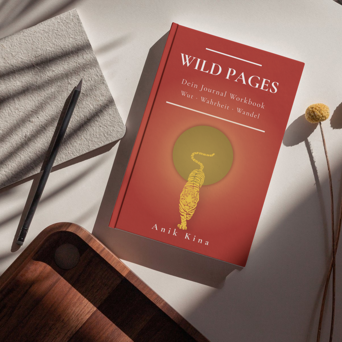 Rotes Buch „Wild Pages“ mit Tiger-Illustration, daneben Stift, graues Tuch und Holztablett auf hellem Hintergrund.
